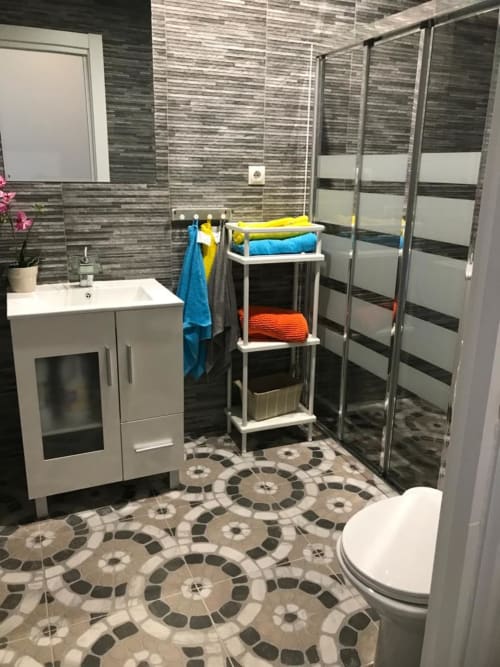 Baño moderno en Apartamentos Huelintown Málaga con azulejos rayados, mampara de ducha de cristal, lavabo blanco y