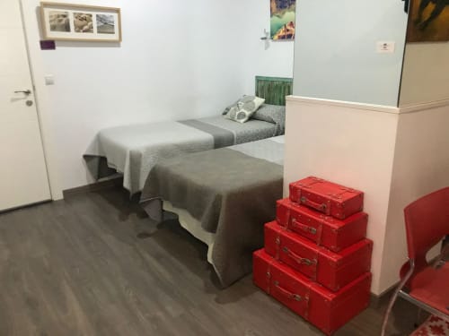 Acogedor dormitorio en Apartamentos Huelintown de Málaga con camas gemelas, maletas rojas y comodidades modernas
