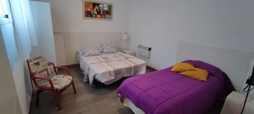 Dormitorio luminoso en Apartamentos Huelintown, Málaga, con cama púrpura, cama blanca, silla roja y comodidades modernas