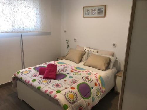 Dormitorio luminoso en Apartamentos Huelintown de Málaga con ropa de cama de colores vibrantes, almohadas beige y cama blanca moderna