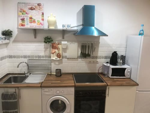 Cocina moderna en Apartamentos Huelintown, Málaga con encimeras de madera, estufa, fregadero, campana extractora azul y electrodomésticos blancos