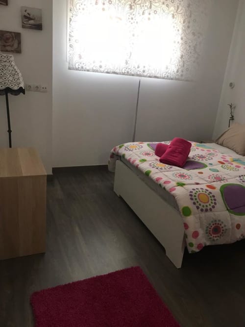 Dormitorio luminoso en Apartamentos Huelintown de Málaga con ropa de cama colorida, escritorio de madera y cortina de encaje.