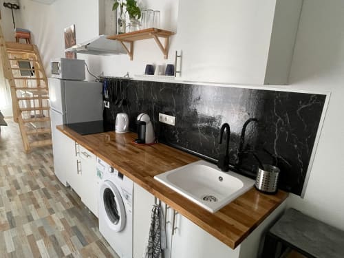 Cocina moderna con encimera de madera, gabinetes blancos, backsplash de mármol negro, fregadero y lavadora en Apartamentos