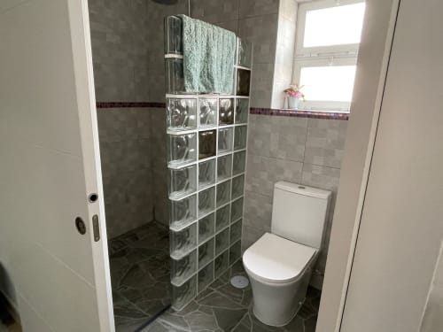 Baño moderno en Apartamentos Huelintown de Málaga con ducha de bloques de vidrio, inodoro blanco y suelo de cerámica.