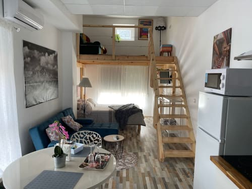 Apartamento estudio compacto en Apartamentos Huelintown, Málaga, con cama tipo loft, cocineta, sofá azul y escaleras de madera