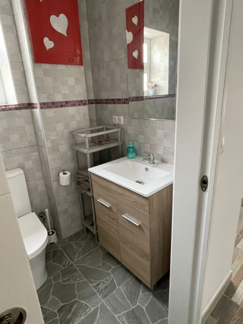 Baño moderno de Apartamentos Huelintown en Málaga con lavamanos blanco, mueble de madera, inodoro y decorativa pared con corazón rojo