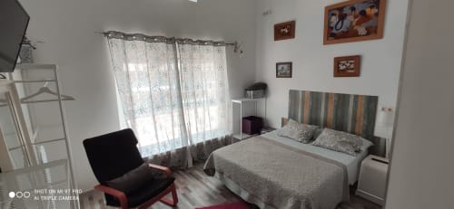 Luminoso dormitorio en Apartamentos Huelintown, Málaga, con cama queen, TV, cabecero a rayas, cortinas de encaje y