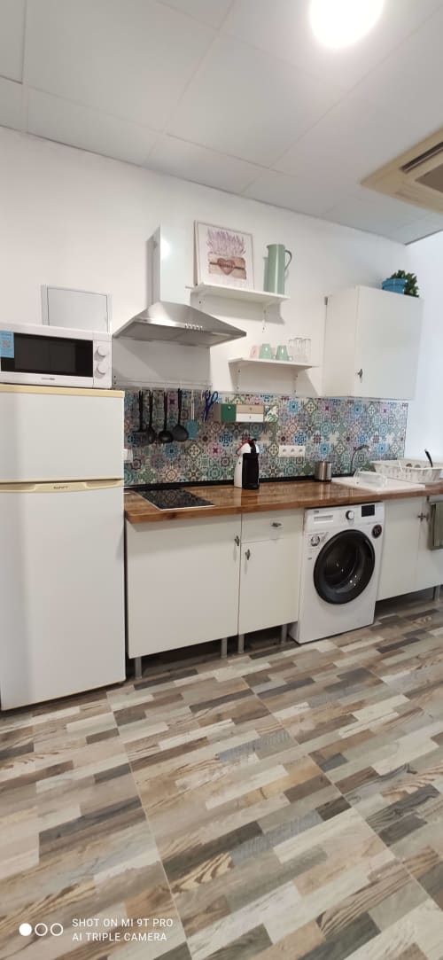 Cocina moderna en Apartamentos Huelintown, Málaga con muebles blancos, encimera de madera, azulejos decorativos y lavadora