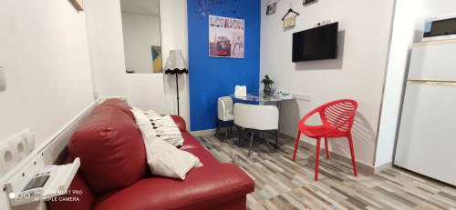 Apartamento moderno en Apartamentos Huelintown, Málaga, con sofá rojo, TV, pared azul y mobiliario contemporáneo
