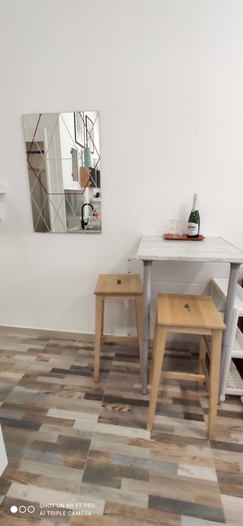 Comedor minimalista con espejo geométrico, mesa de mármol, taburetes de madera y champagne en Apartamentos