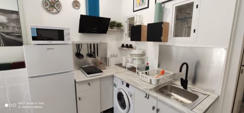Cocina moderna del apartamento en Huelintown Málaga con electrodomésticos blancos, lavadora, fregadero, placa de cocción y estanterías de almacenamiento