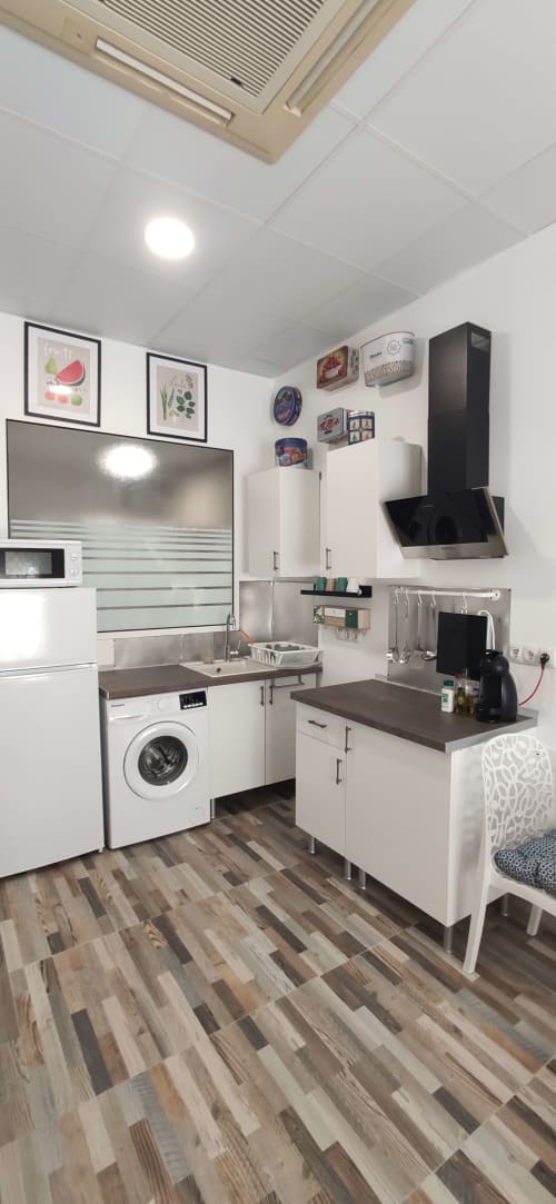 Moderno área de cocina en apartamento Huelintown con muebles blancos, lavadora y piso de madera oscura