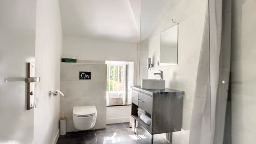 Salle de bains moderne de l'appartement Résidence L'Hermitière avec toilettes, vasque noir mat, miroir et douche vitrée
