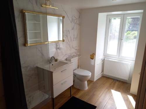 Salle de bain moderne à la Moulin de la Chevanne avec murs en marbre, vasque, toilettes et douche vitrée avec finitions laiton