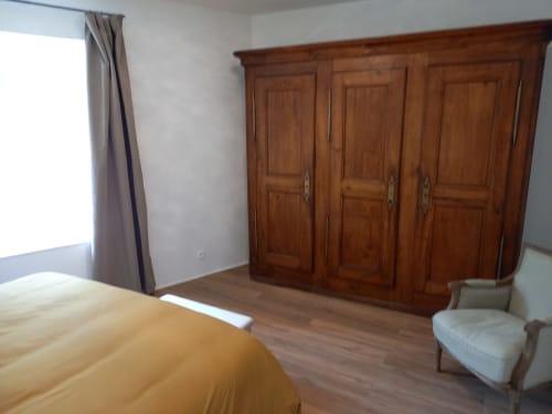 Chambre spacieuse avec armoire en bois, lit jaune, fenêtre avec rideaux et fauteuil au Moulin de la Chevanne B&B