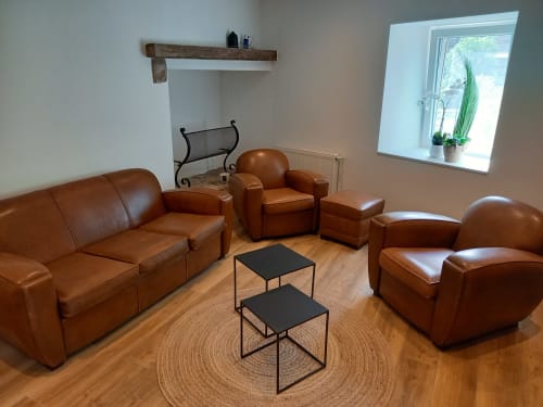 Salon moderne avec sièges en cuir cognac, tables d'appoint noires et parquet au Moulin de la Chevanne à Champlive
