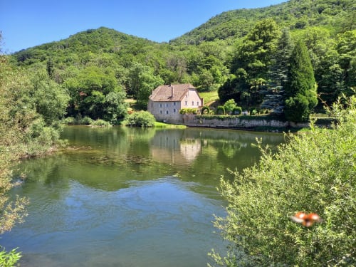 Moulin de la Chevanne, gîte au bord de la rivière avec bâtisse en pierre reflétée dans l'eau calme, entouré de collines verdoyantes à Champlive.