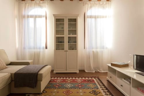 Bright Venetian apartment living room with cream sofa, glass cabinet, patterned rug, and sheer curtains at Ca Cortigiane,