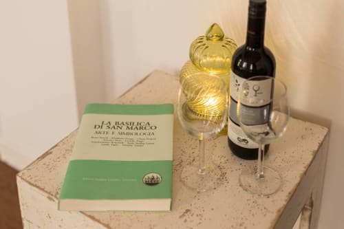 Bedside table at Ca Cortigiane Venice apartment with wine bottle, glass, decorative jar, and book about Basilica di San Marco