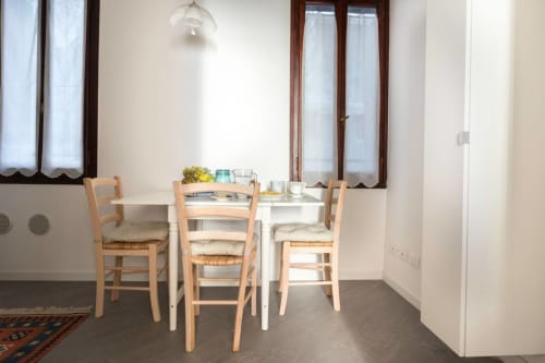 Bright dining area in Ca Cortigiane Venice apartment with white table, wooden chairs, and windows overlooking the city