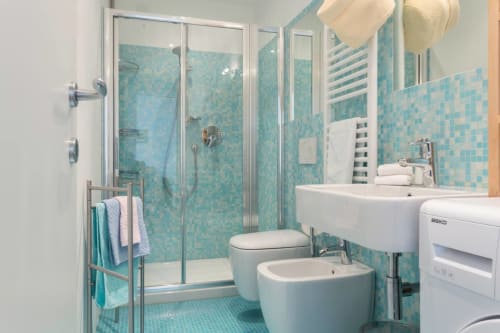 Modern turquoise tiled bathroom with walk-in shower, dual sinks, and toilet at Ca Cortigiane apartment in Venice