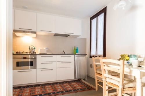 Modern white kitchen with stainless steel appliances, dining table, and chairs in Ca Corrigiane apartment, Venice