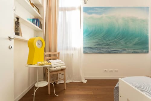 Bright bedroom in Venice apartment with yellow clock, ocean wave artwork, wooden floor, and coastal decor