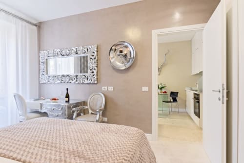 Camera da letto di Petra Apartments Roma con specchio ornato, scrivania e cucina en-suite visibile attraverso la porta