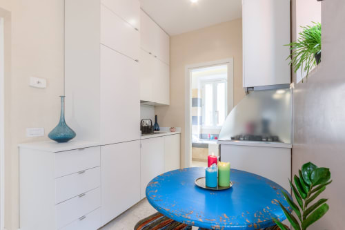 Cucina moderna bianca a Petra Apartments Roma con tavolo rotondo blu, elettrodomestici in acciaio inox e piante verdi