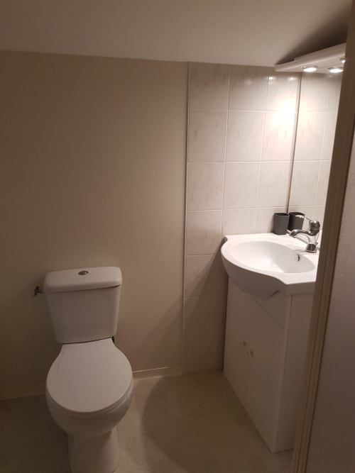 Salle de bain moderne et épurée avec toilettes blanches, lavabo sur colonne et murs carrelés à la maison d'hôtes Le Pommier