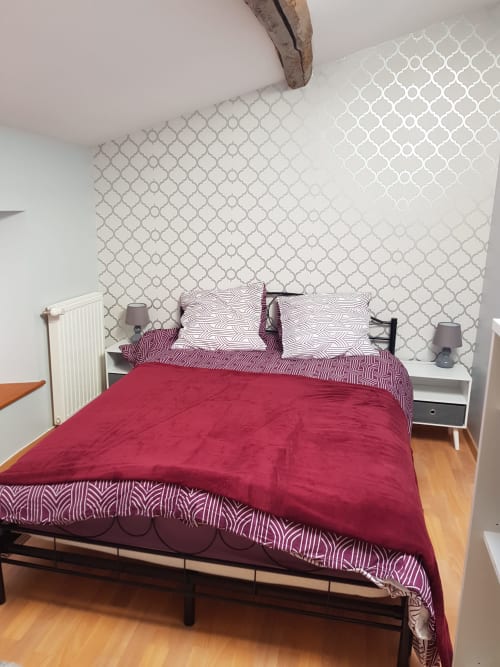 Cozy bedroom at Le Pommier B&B with burgundy bedding, geometric wallpaper, and white nightstands