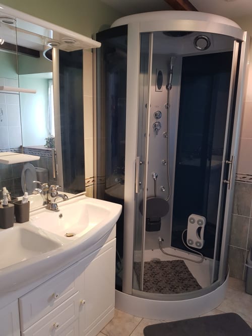 Salle de bain moderne au gîte Le Pommier avec lavabo blanc, miroir et cabine de douche avec hammam d'angle