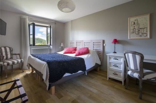 Chambre lumineuse à La Maison De Siloe avec lit, oreillers roses, bureau et vue sur les montagnes à Villefranche de Rouergue