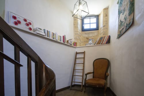 Palier d'escalier à La Maison De Siloe avec échelle en bois, fauteuil marron, étagères flottantes et suspension géométrique