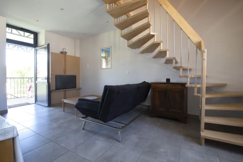 Espace de vie cottage moderne à La Maison De Siloe avec escalier flottant en bois, fauteuil noir, TV et accès au balcon