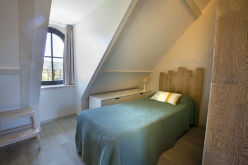 Chambre lumineuse sous les combles à La Maison De Siloe à Villefranche de Rouergue, avec lit vert, tête de lit en bois et plafond voûté