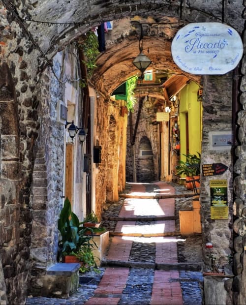 Charmante ruelle en pierre à Dolceacqua, Italie avec passage voûté, porte jaune et architecture traditionnelle