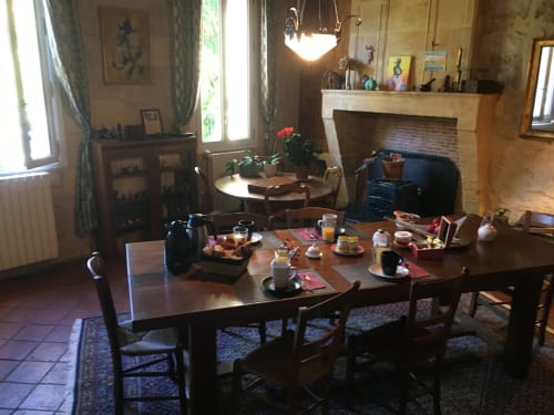 Salle à manger rustique de la chambre d'hôtes Sous Les Marronniers avec grande table en bois dressée pour le petit-déjeuner, cheminée et charme à Petit Palais
