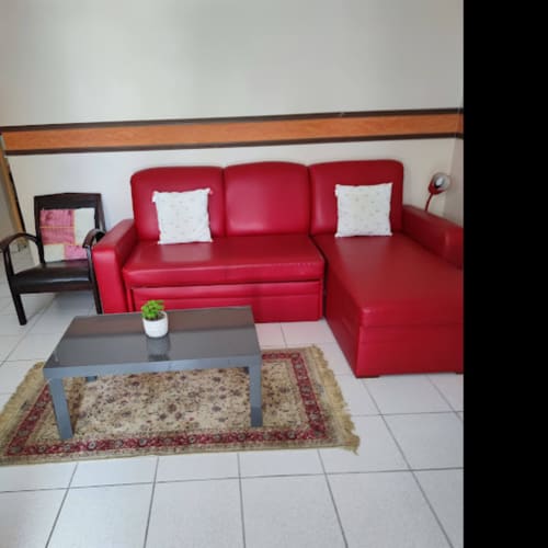 Canapé sectionnel rouge moderne avec coussins blancs dans le salon meublé de la Résidence Les 2 Moulins, Guadeloupe.
