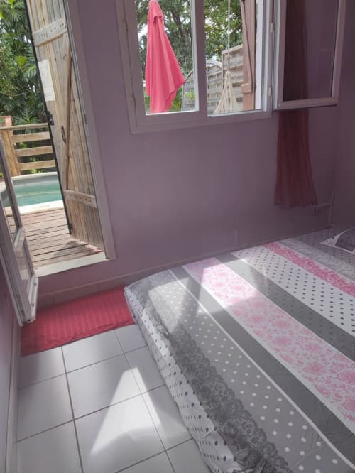 Chambre lumineuse à la Résidence Les 2 Moulins en Guadeloupe avec carrelage, tapis colorés et accès balcon à la piscine