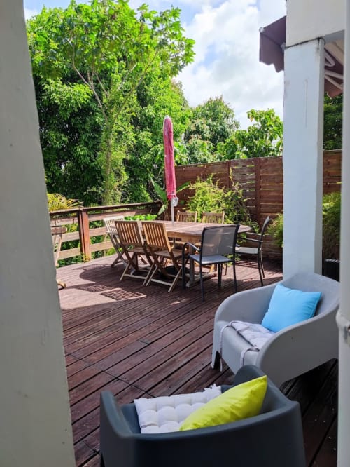 Balcon tropical de la Résidence Les 2 Moulins avec salon, table à manger et vue sur le jardin luxuriant en Guadeloupe