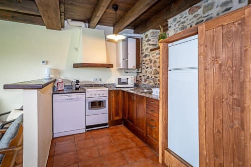 Cocina rústica en villa Torre Gelbert, Puigcerdà con vigas de madera, muros de piedra y pavimento de terracota