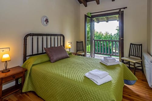 Dormitorio luminoso en Torre Gelbert con ropa de cama verde, vistas a las montañas desde el balcón, suelos de madera y estilo tradicional