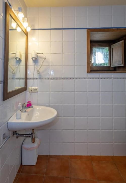 Baño de la villa Torre Gelbert en Puigcerdà con paredes de azulejos blancos, espejo con marco de madera y lavabo