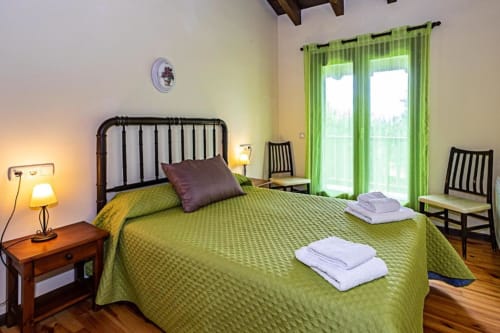 Dormitorio luminoso en Torre Gelbert con ropa de cama verde lima, cama de hierro forjado, cortinas verdes y vistas a la montaña