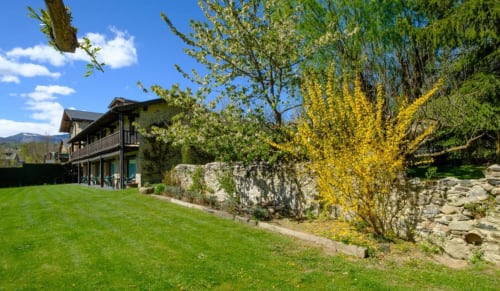 Villa Torre Gelbert en Puigcerdà con jardín cuidado, plantas florales amarillas, muros de piedra y vistas montañosas en primavera