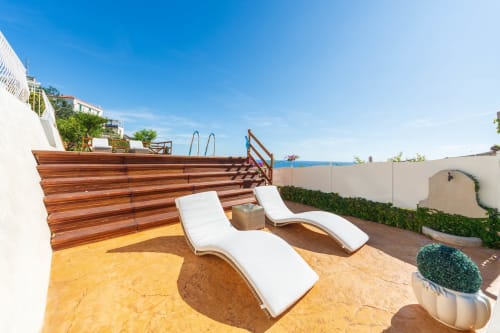 Terrazza soleggiata di Villa Costanza con due lettini bianchi, pannello in legno per la privacy e vista mare a Maiori