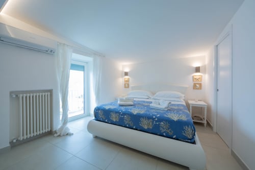 Camera moderna a Villa Costanza sulla Costiera Amalfitana con vista mare, biancheria blu, cuscini bianchi e accesso al balcone