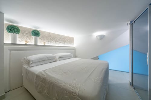 Camera moderna a Villa Costanza sulla Costiera Amalfitana con letto bianco, piante verdi in vaso e finestra con vista sul mare azzurro