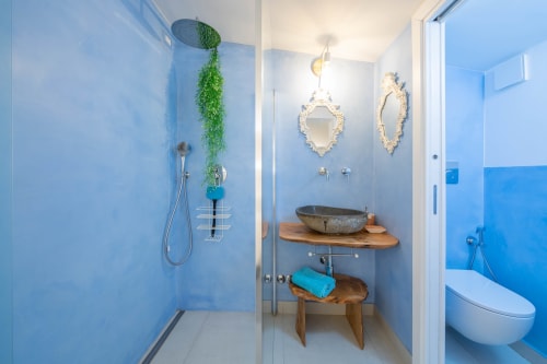 Bagno moderno di Villa Costanza sulla costa amalfitana con doccia piastrellata blu, lavabo in pietra, piante sospese e specchi decorativi